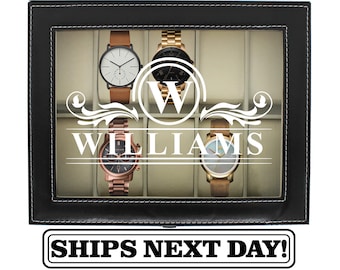 May include: A black rectangular watch display case with a glass lid featuring a white monogram W and the name WILLIAMS printed on the center. The interior contains beige velvet cushions holding four wristwatches with various metal and leather bands.