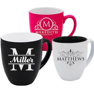 May include: Three ceramic mugs in pink, black, and white. Each mug features a different personalized design with a name and initial. The pink mug has the name "Meredith", the black mug has "Miller", and the white mug has "Matthews".