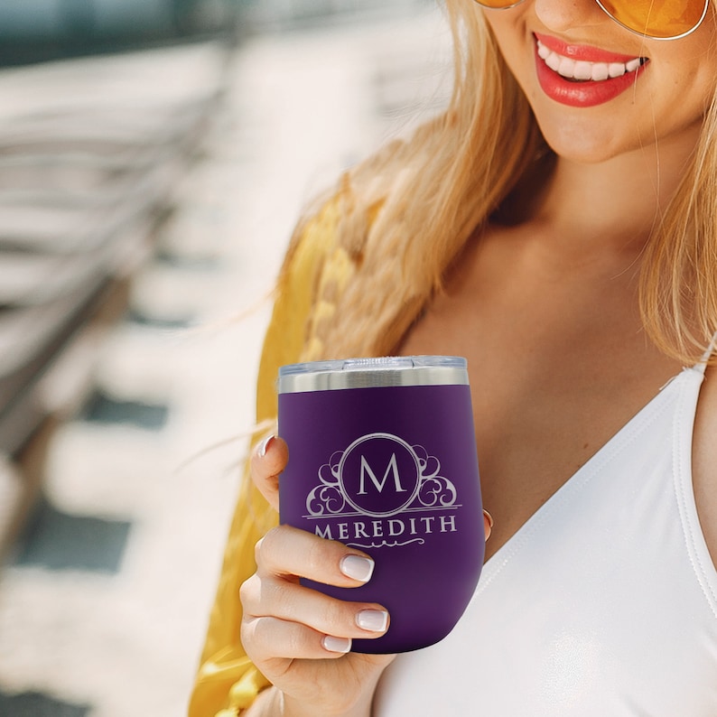 May include: A purple insulated wine tumbler with a silver rim and lid. The tumbler features a monogram with the letter "M" inside a decorative circle, and the name "MEREDITH" below. The tumbler is held by a person.