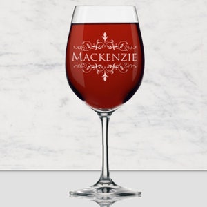 May include: A clear glass wine glass filled with deep red liquid. The glass features a white etched design consisting of symmetrical floral scrollwork above and below the name MACKENZIE, which is printed in a clean, white, capitalized font.