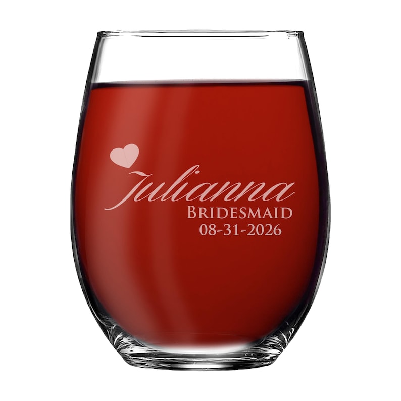 May include: A clear stemless wine glass filled with red liquid, featuring white etched text that reads Julianna, BRIDESMAID, and 08-31-2026, accompanied by a small white heart icon positioned above the name on the front of the glass.