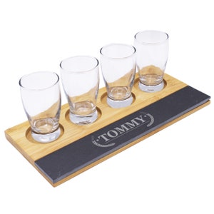 May include: A wooden beer flight set with four clear glass tasting glasses. The set includes a bamboo base with a dark gray slate insert. The word "TOMMY" is engraved on the slate.