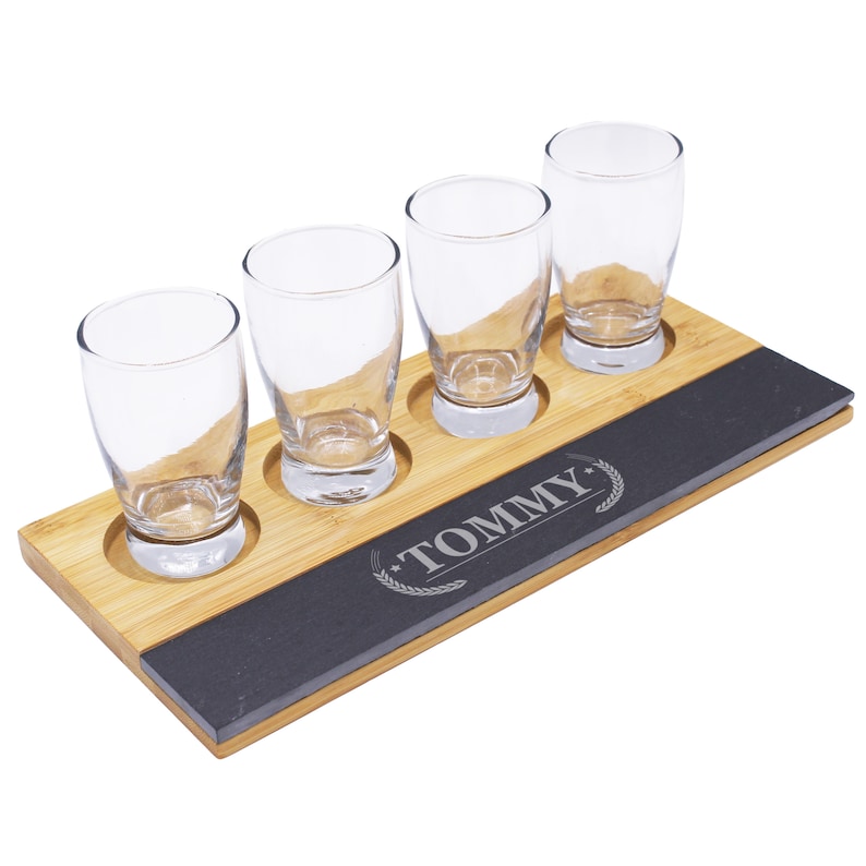 May include: A wooden beer flight set with four clear glass tasting glasses. The set includes a bamboo base with a dark gray slate insert. The word "TOMMY" is engraved on the slate.