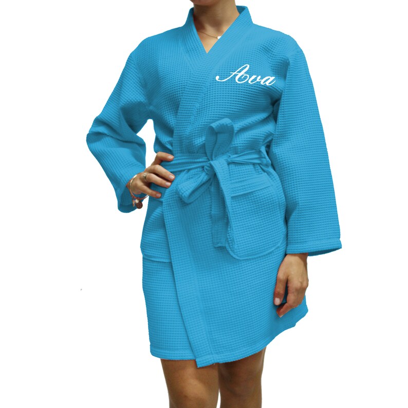 May include: A light blue waffle weave robe with a white embroidered name "Ava" on the left chest.