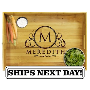 May include: A rectangular bamboo serving tray featuring a dark brown laser-engraved monogram with the letter M inside a circular frame above the name MEREDITH. The tray contains a small bowl of white dip, a small bowl of green arugula, and three carrots.