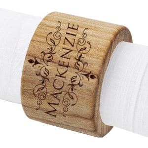 May include: A wooden napkin ring with the name "Mackenzie" engraved on it. The ring is brown and has a decorative design.