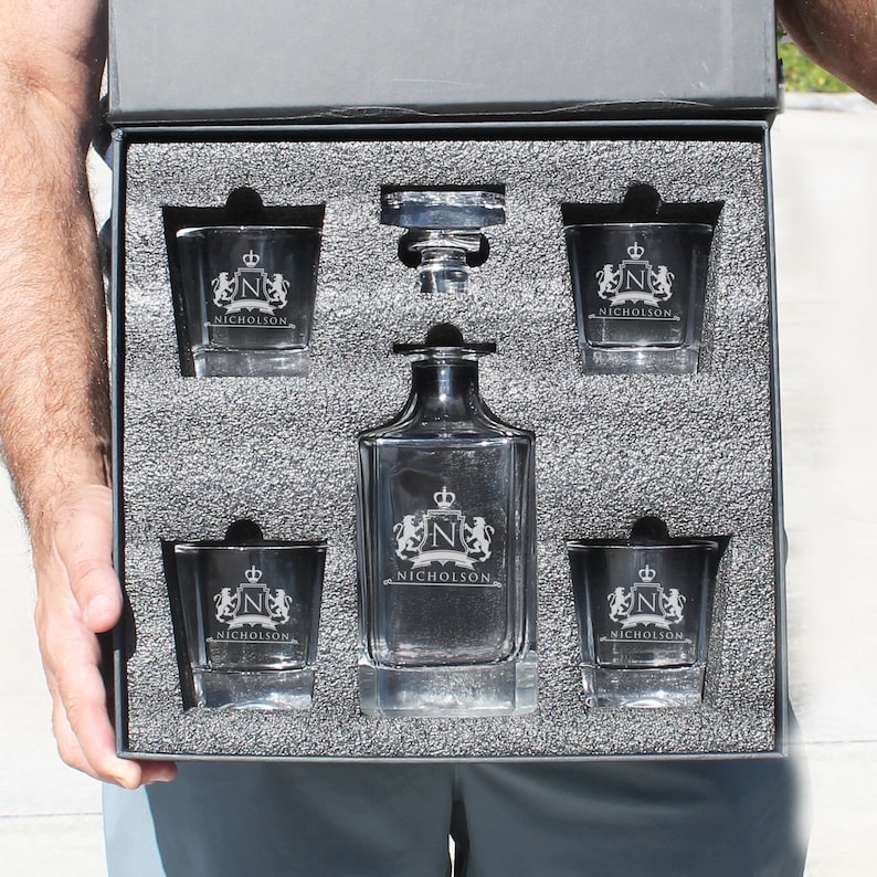 Peut inclure: Une carafe en verre transparent et quatre verres assortis dans une bo&icirc;te doubl&eacute;e de mousse noire. Chaque pi&egrave;ce pr&eacute;sente un blason grav&eacute; avec une couronne, la lettre N et le nom NICHOLSON. La carafe inclut un bouchon en verre et les verres sont carr&eacute;s.