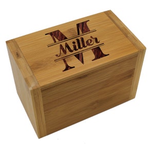 Puede incluir: Una caja de almacenamiento rectangular de bamb&uacute; con tapa abatible. La parte superior de la tapa presenta un dise&ntilde;o grabado con l&aacute;ser que consiste en una letra M grande, el nombre Miller en cursiva y otra letra M grande centrada.