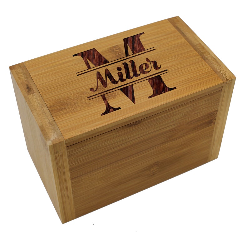 Puede incluir: Una caja de almacenamiento rectangular de bamb&uacute; con tapa abatible. La parte superior de la tapa presenta un dise&ntilde;o grabado con l&aacute;ser que consiste en una letra M grande, el nombre Miller en cursiva y otra letra M grande centrada.