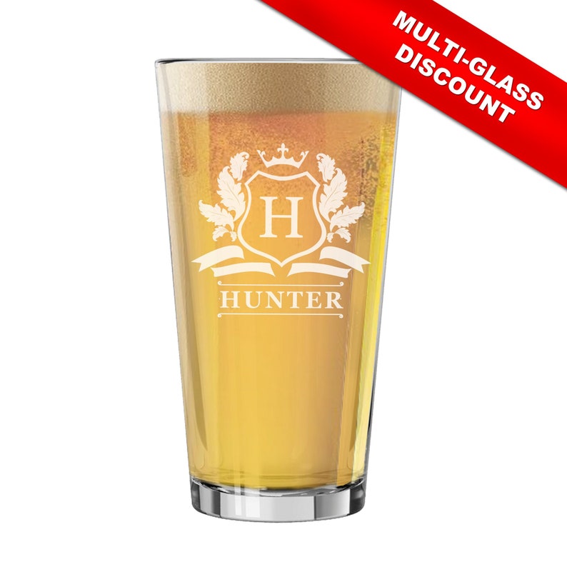May include: A clear pint glass filled with beer and foam. The glass features an etched crest design with the letter "H" and the name "HUNTER" below. A red banner in the corner reads "MULTI-GLASS DISCOUNT".
