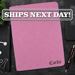 May include: A rectangular pink portfolio case with rounded corners and visible stitching along the edges. The name Carlie is printed in a dark, stylized serif font in the bottom right corner. The text SHIPS NEXT DAY is visible at the top.