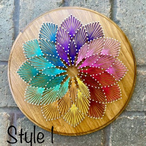 May include: A colorful string art mandala with a rainbow color scheme. The mandala is created with string wrapped around nails hammered into a wooden circle. The background is a brick wall.