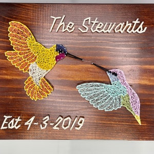 May include: A wooden sign with two hummingbirds made of string art. The hummingbirds are facing each other and the sign says "The Stewarts Est 4-3-2019".