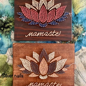 May include: Two wooden signs with a string art lotus flower design. The top sign has copper nails and the bottom sign has silver nails. Both signs have the word "namaste" written below the flower.