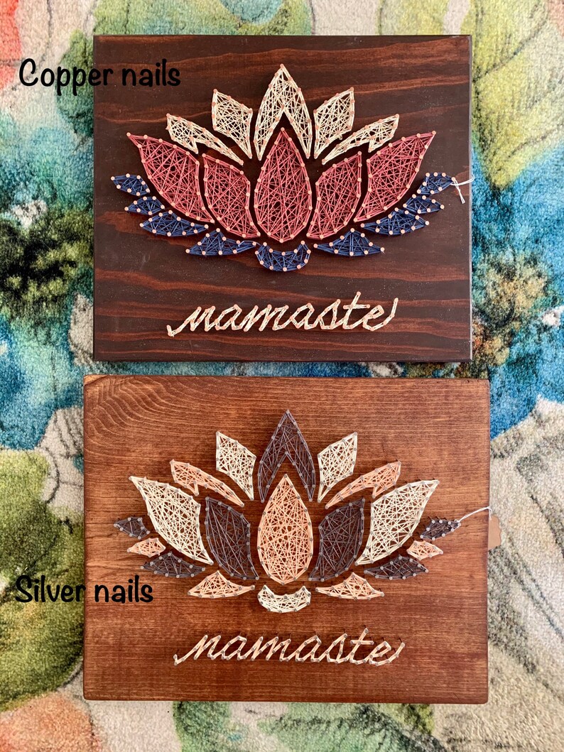May include: Two wooden signs with a string art lotus flower design. The top sign has copper nails and the bottom sign has silver nails. Both signs have the word "namaste" written below the flower.