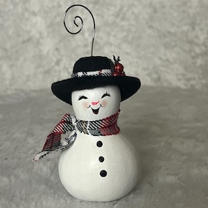 Snowman ornament with felt top hat, adorned with greens and berries.  He is made out of a natural dried and preserved gourd.