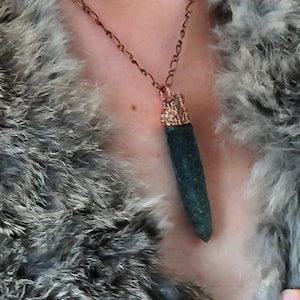 Puede incluir: Una mujer con un abrigo de piel gris con un collar de cadena de cobre y un colgante de piedra verde oscuro.