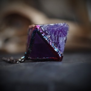 Puede incluir: Un colgante de cristal morado con un envoltorio de alambre metálico plateado y rojo. El colgante está unido a una cadena plateada.
