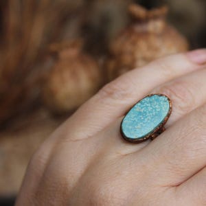 May include: A turquoise oval ring with a copper wire setting. The ring is on a person's finger.