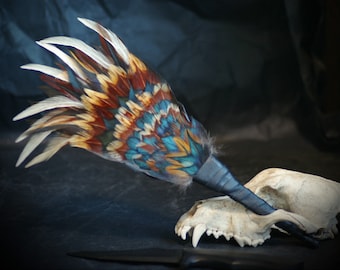 May include: A colourful feather fan with a black leather handle, resting on a white animal skull.