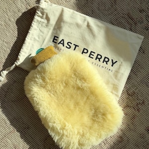 May include: A yellow sheepskin hot water bottle cover and a cream-colored drawstring bag. The bag is printed with "EAST PERRY" in black. The hot water bottle cover has a fluffy, soft texture.