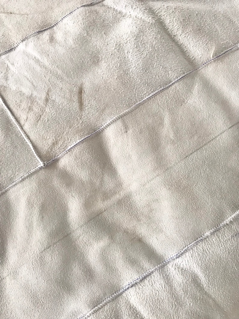 Pode incluir: Um cobertor branco de pel&uacute;cia acolchoado com uma textura macia e felpuda. O cobertor &eacute; feito de v&aacute;rios pain&eacute;is costurados juntos, criando um efeito de patchwork.