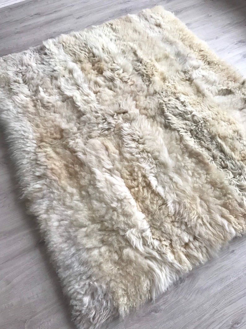 Pode incluir: Um tapete de pele de carneiro branco com uma textura macia e fofa. O tapete &eacute; feito de pele de carneiro natural e tem uma cor bege claro.