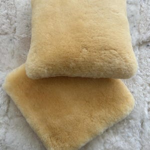 May include: Two soft, fluffy, cream-colored sheepskin throw pillows. The pillows are made of natural sheepskin and have a luxurious feel.
