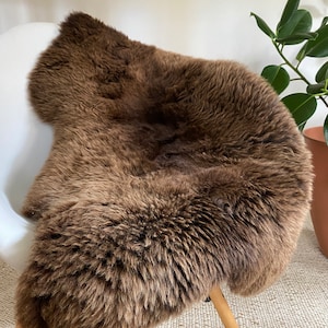 May include: A brown sheepskin rug draped over a wooden chair. The rug has a soft, fluffy texture and is perfect for adding warmth and comfort to any room.