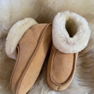 May include: A pair of tan suede slippers with a white sheepskin lining. The slippers have a simple design and are perfect for keeping your feet warm in the winter.