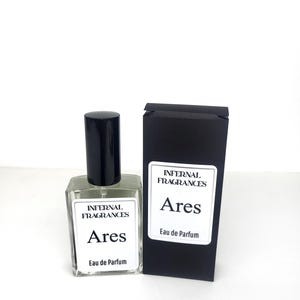 Puede incluir: Una etiqueta en blanco y negro en una botella de perfume de vidrio transparente que dice "Internal Fragrances Ares Eau de Parfum". La botella est&aacute; junto a una caja negra con la misma etiqueta.