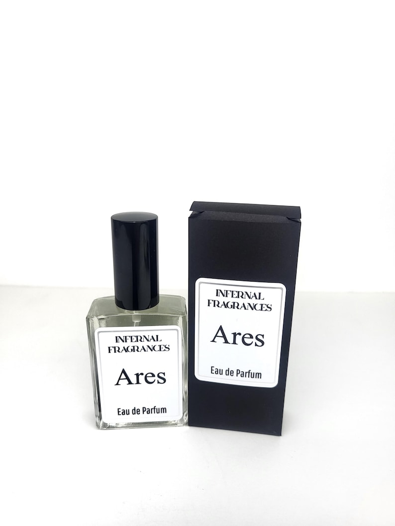 Puede incluir: Una etiqueta en blanco y negro en una botella de perfume de vidrio transparente que dice "Internal Fragrances Ares Eau de Parfum". La botella est&aacute; junto a una caja negra con la misma etiqueta.