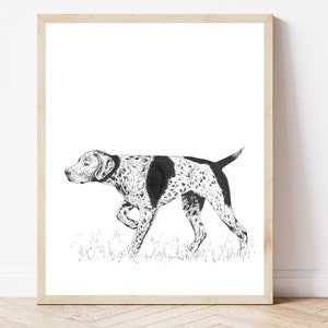 Op de afbeelding: Zwart-witte inkttekening van een hond in een houten lijst. De hond, een pointerras, heeft een gevlekte vacht en een zwarte vlek op zijn rug. De hond loopt over gras.