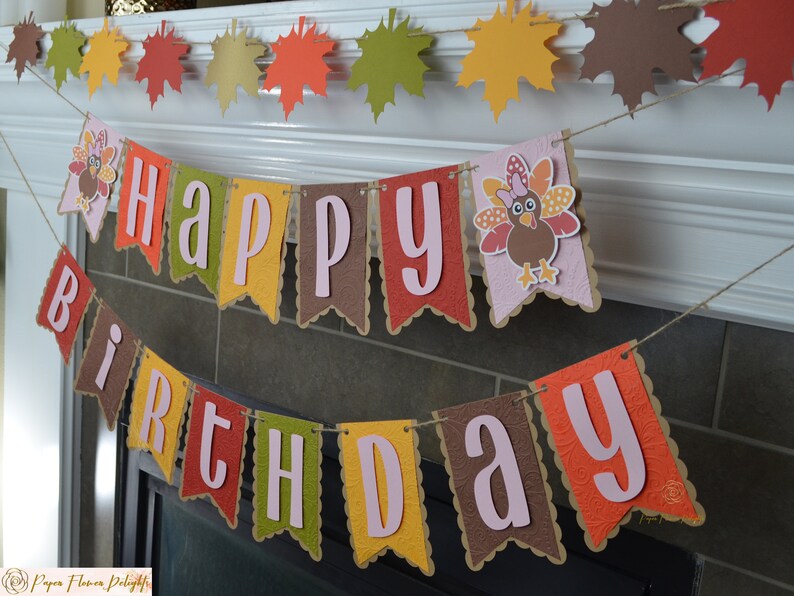 May include: A festive banner with the words "Happy Birthday" in pink letters on brown, orange, yellow, and green pennants. A turkey with a pink bow is on one of the pennants.