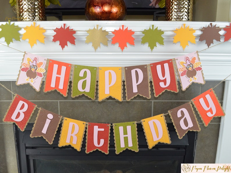 May include: A festive fall-themed birthday banner with the words "Happy Birthday" in pink letters on brown, orange, yellow, and green pennants. The banner is decorated with images of turkeys and fall leaves.