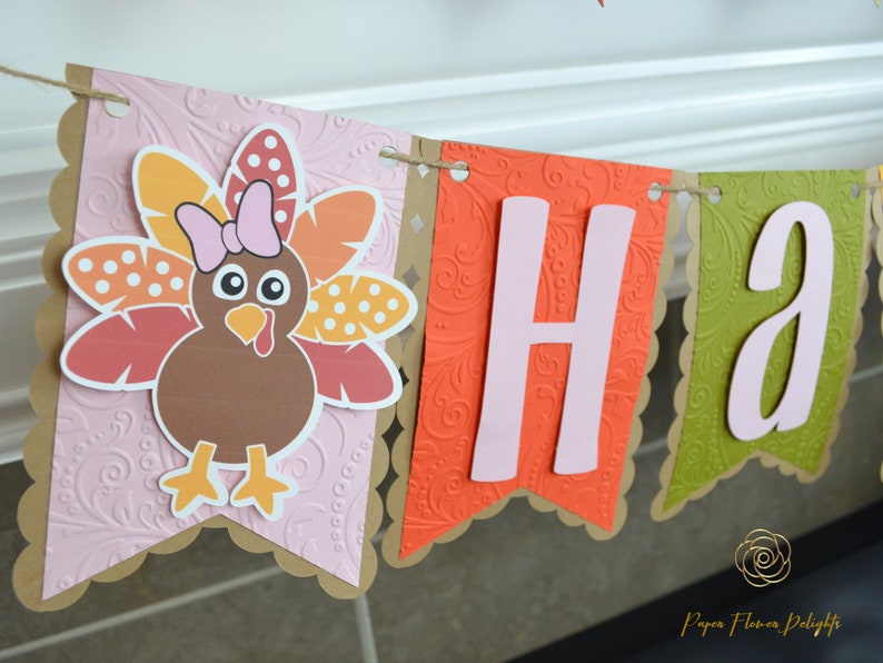 May include: A Thanksgiving banner with the word "Happy" in pink letters on a brown, orange, and green background. The banner features a cute cartoon turkey with a pink bow.