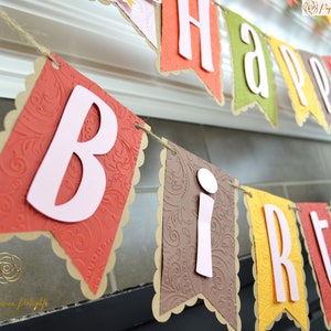 May include: A brown, orange, yellow, and green paper banner with the words "Happy Birthday" in white letters. The banner is decorated with a paisley pattern.