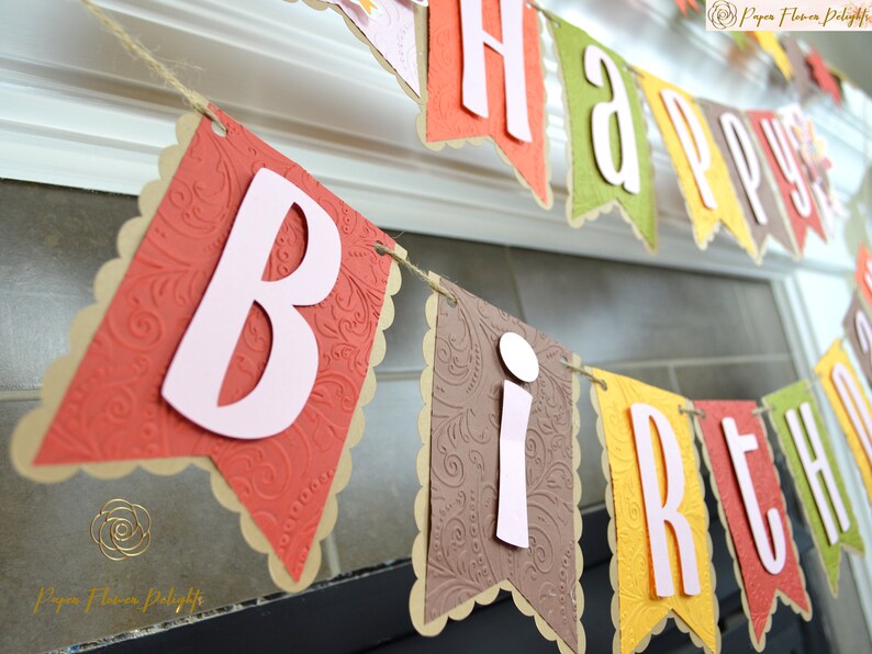 May include: A brown, orange, yellow, and green paper banner with the words "Happy Birthday" in white letters. The banner is decorated with a paisley pattern.