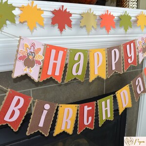 May include: A brown, orange, and green banner with the words "Happy Birthday" in pink letters. The banner is decorated with fall leaves and turkeys.