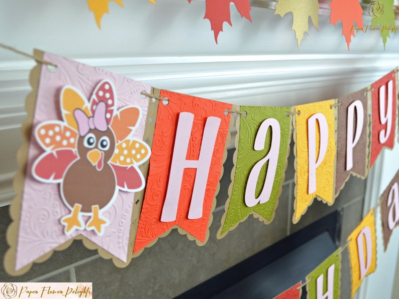 May include: A pink, orange, and brown paper banner with the word "HAPPY" in pink letters. The banner is decorated with a brown turkey with pink feathers and a pink bow.