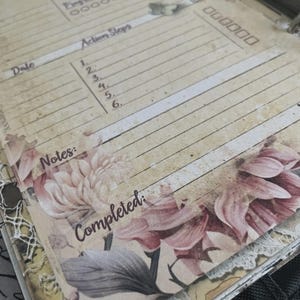 May include: A vintage-style journal page with lined sections for notes and action steps. The page features floral illustrations in shades of pink and gray, with the word "Completed" at the bottom. The overall design has a distressed, aged appearance.