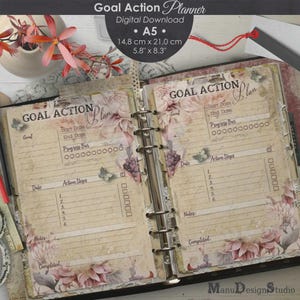 May include: Open A5 goal action planner with floral and butterfly accents. The planner is open to two pages, featuring sections for goals, dates, action steps, and progress bars. The planner measures 5.8" x 8.3".