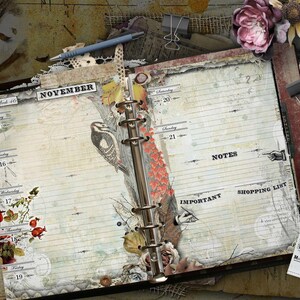 An open ring-bound planner with cream-colored pages featuring a November calendar layout. The pages include illustrations of a bird, berries, and floral elements, with printed text labels for days, notes, important, and shopping list.