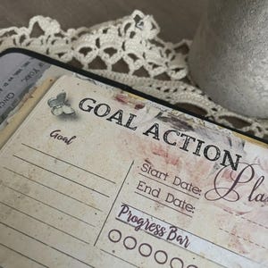 May include: A vintage-style planner page with the words "GOAL ACTION Plan" in black lettering. The page has a floral design and a butterfly illustration. It includes sections for start and end dates, and a progress bar.