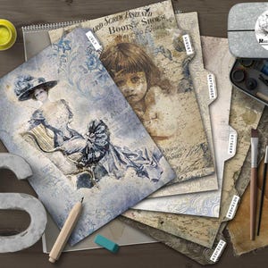 May include: A collection of vintage-style paper ephemera, including pages with illustrations and text, arranged on a wooden surface. Art supplies like paint, brushes, and a pencil are also present, along with a metal container with a logo.