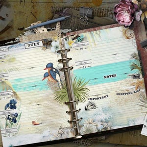 An open ring-bound planner featuring a July calendar layout with beach-themed illustrations, including birds, palm leaves, and seashells. The pages contain printed text for days of the week, notes, shopping list, and important sections.