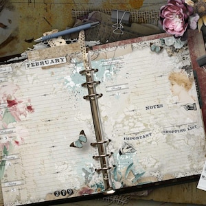 May include: An open ring-bound planner with cream-coloured pages featuring the text February, Week 5, Notes, Important, and Shopping List. The pages are decorated with vintage-style illustrations of flowers, a butterfly, and a person, alongside a blue pen, scissors, a feather, and cotton stems.