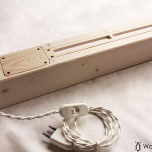 May include: A wooden light fixture with a white cord and plug. The fixture has a rectangular shape and a light switch on the cord. The fixture is made of natural wood and has a simple design.