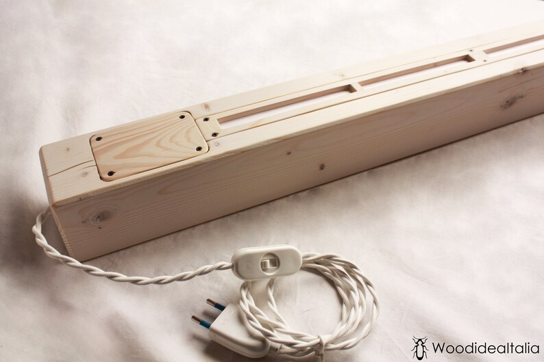 May include: A wooden light fixture with a white cord and plug. The fixture has a rectangular shape and a light switch on the cord. The fixture is made of natural wood and has a simple design.
