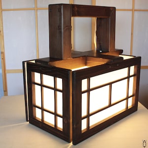 May include: A dark brown wooden lantern with a rectangular shape and a grid pattern on the front. The lantern has a handle on the top and is lit from within, casting a warm glow.